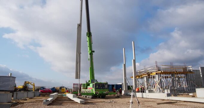 Crane and construction workers erect a precast structural column as part of an industrial building frame. Site preparation, safety gear, and teamwork are visible in this phase of concrete assembly.