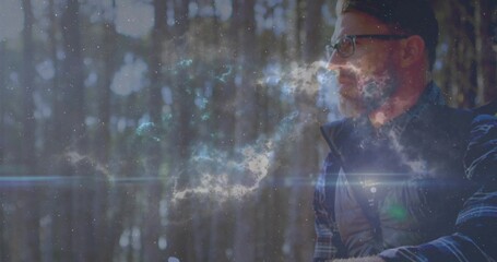 Sitting man gazing ahead in pine forest, with quilted vest, plaid shirt, eyeglasses, copy space