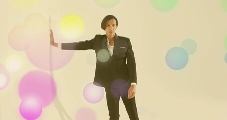 Posing Asian model extending left arm on white vertical panel in cream studio, with pastel circles