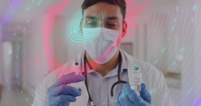 Medical doctor wearing lab coat preparing vaccine in treatment room, with COVID-19 vial and syringe