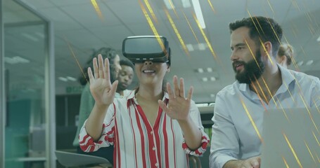 Woman wearing VR headset interacting in open-plan office, with laptops, monitors and tablet
