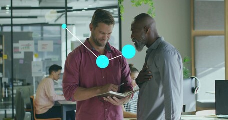 Reviewing notebook, two male colleagues collaborating in modern office with computers and plants