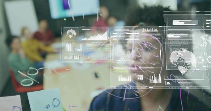 Studying man with glasses examining overlays on glass board in meeting room, with laptops mugs