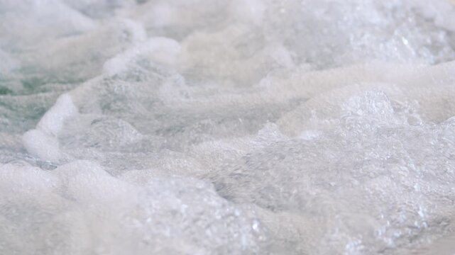 Slow motion view of bubbling water and foam in a jacuzzi, showing dynamic movement, texture, and energy. Air jets create a relaxing, invigorating spa effect with swirling bubbles.