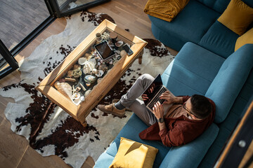 Obraz premium Man working remotely on laptop from home couch