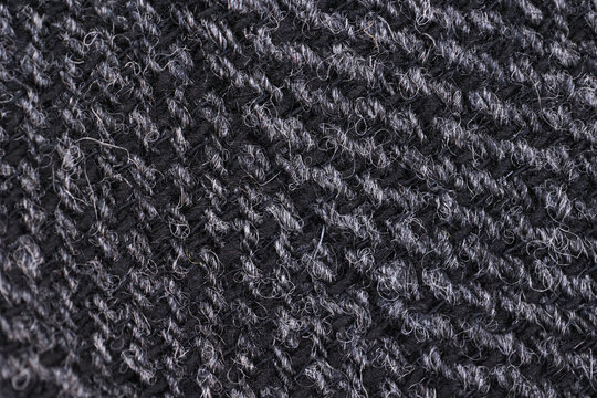 Extreme close-up macro shot of dark gray English tweed wool fabric. Shows the classic herringbone weave texture, natural fibers, and soft, durable textile material. Ideal for fashion and tailoring.