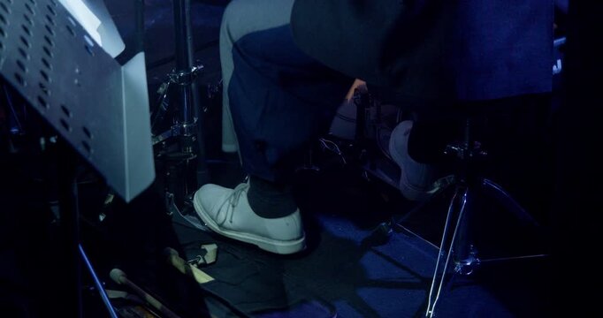 Dynamic close-up shows a jazz drummer&rsquo;s feet operating bass drum and hi-hat pedals during a concert. Drumsticks and stand details add context to the live rhythm section performance.