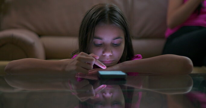 Teenager sitting on couch with smartphone, scene pans to young girl on floor staring at screen, highlighting technology addiction and digital dependence in children