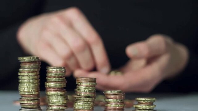 Stock image of a hand holding coins above a pile of coins on a table, illustrating finance, business, and growth concepts like savings and investment