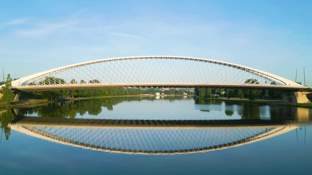 Experience the beauty of Troja Bridge in Prague as the morning sun casts a warm glow on its elegant design above the calm waters of the Vltava River. Nature and architecture unite.