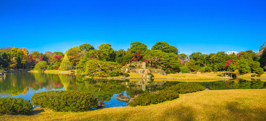 Panoramic view of a traditional Japanese garden with colorful autumn trees reflecting in a pond (Rikugien Garden, Tokyo, Japan)