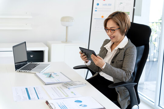 Asian professional woman conducting business analysis with digital tablet laptop modern office setting work productivity happy focused financial data review