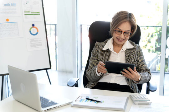 Asian adult businesswoman using digital tablet for work office setting analyzing business data marketing reports preparing financial strategy remote work solution