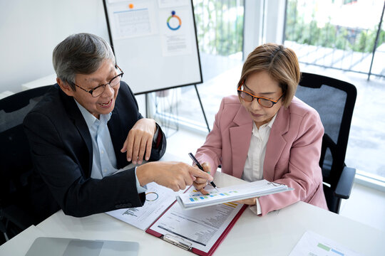Asian adult business professionals discussing financial reports data analysis strategy in modern office meeting room collaborating on growth plans