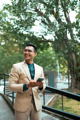 Obraz premium Asian businessman using smartphone, smiling in park