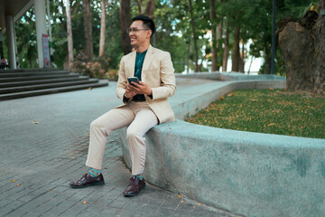 Obraz premium Stylish Asian man sitting outdoors using phone