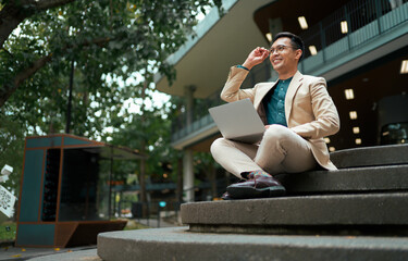 Asian businessman using laptop outdoors feeling successful