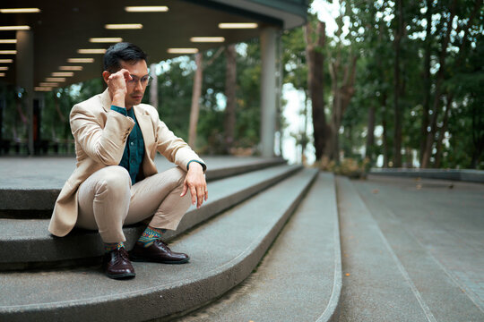 Asian man sitting on stairs thinking about problems