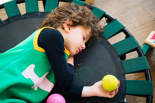Autistic young girl sleeping on rebounder trampoline with toys, experiencing exhaustion and peaceful rest