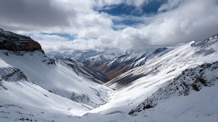 Majestic snow covered mountain range extends into a deep valley beneath dynamic clouds