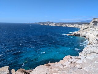 view of the medieval town of Bonifacio with its white limestone coastline and rough, deep blue turquoise sea in sunshine and blue skies	