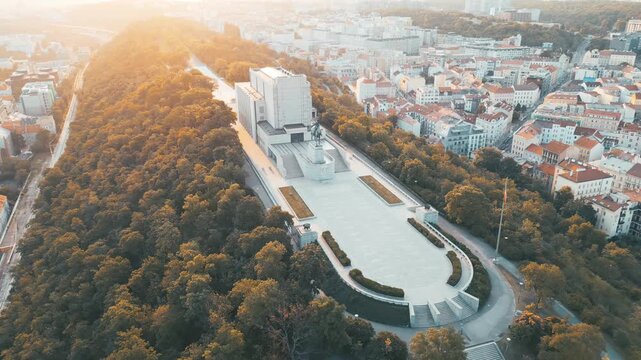 Witness the stunning sunrise over the National Monument at Vitkov Hill. This early morning view showcases Jan Zizka's Statue surrounded by lush greenery and the beautiful skyline of Prague.