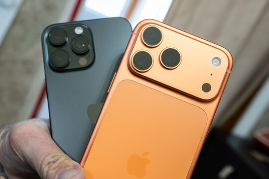 hand holds the new iPhone 17 Promax  in cosmic orange and the older iPhone 16 Promax illustrating evolving trends in mobile technology and consumer choice and showcasing contrasting design style