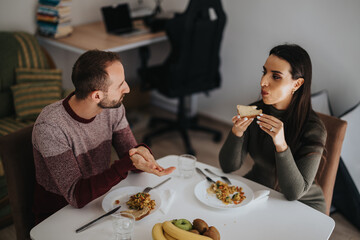 A man and woman share a meal at a dining table, engaging in conversation, creating a warm and intimate atmosphere in a modern home setting.
