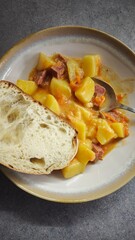 Plate of homemade stewed potatoes with meat and vegetables served with a slice of bread. The image conveys the concept of comfort food and traditional homemade meal
