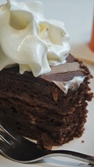 Slice of rich chocolate cake with whipped cream topping served on a plate. The image conveys the concept of indulgence, celebration, and sweet dessert pleasure