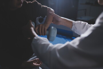 Old woman training with physiotherapist using dumbbells at home. Therapist assisting senior woman with exercises in nursing home. Elderly patient using dumbbells with outstretched arms.