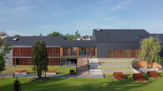 Aerial lateral movement along modern slate and timber-clad public pool, Eisenberga Street Krakow, with sun lounges in landscaped park setting.