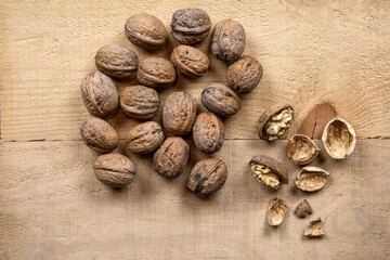 On a rustic wooden board, fresh organic walnuts from our own garden lie scattered. Some are cracked open, revealing their golden brown core. A true taste of nature, full of flavor and quality.