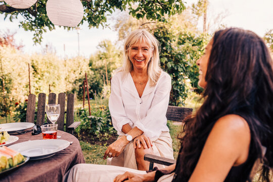Happy senior woman talking with female friend while sitting at dining table in back yard