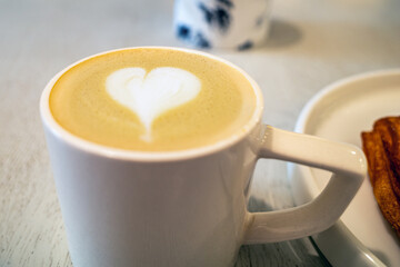 Close-up of a white ceramic mug filled with a latte, adorned with a latte art heart.