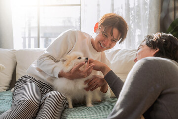 An LGBTQ male couple enjoys a tender and loving moment at home, relaxing together on the sofa with their adorable Pomeranian dog. Surrounded by warmth and affection, they share a peaceful lifestyle 