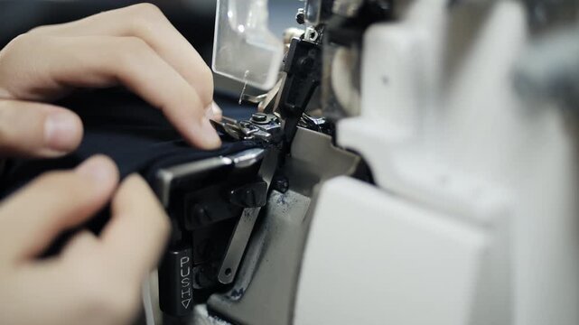 Hands guiding fabric through industrial overlock machine during stitching