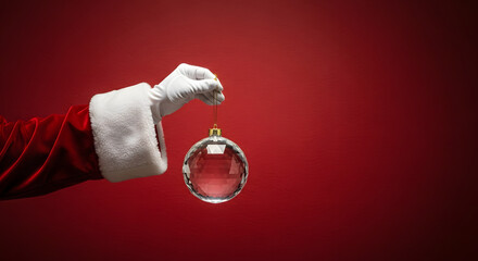 Santa's hand holding transparent ball Christmas decoration on red background.