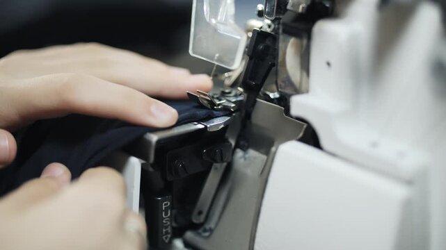 Seamstress operating industrial overlock machine while stitching fabric