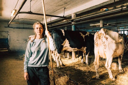 Portrait of female cattle worker holding pitchfork with cows in background