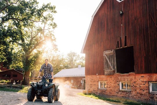Farmer driving quadbike at farm during sunny day