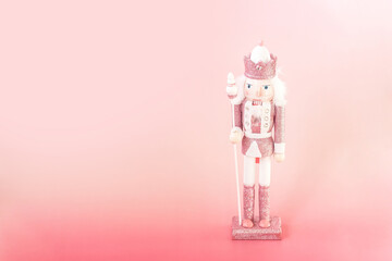 Stylish pink nutcracker figurine standing on a pink background beside small star-shaped cookies,...