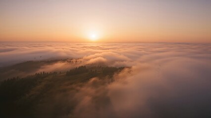 Obraz premium Sunrise over a foggy landscape with the sun just above the horizon and clouds covering the terrain.