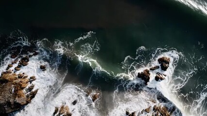 Aerial view of a rocky coastline with dark green sea and white foamy waves crashing over the rocks. - Powered by Adobe