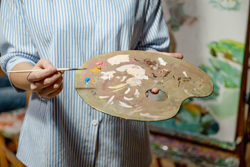 Artist holding a paint palette and brush, preparing to create artwork. Close-up of colorful oil paints on palette, creative studio atmosphere.
