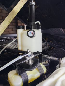 A pressure brake bleeder container standing in the engine bay of an old car, connected by a tube and adaptor to the fluid reservoir, allowing air to be bled from the brake system without an assistant.