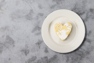 Heart shaped cookie lying on white plate on textured stone background