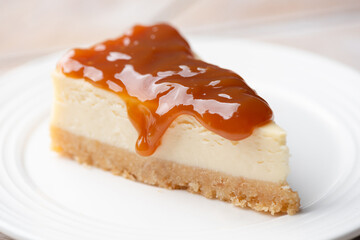 Cheesecake slice with caramel sauce topping on a white dessert plate, closeup view