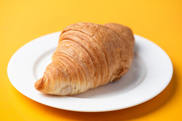 Delicious french croissant on white plate, yellow background