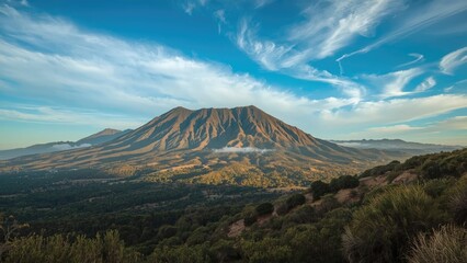Fototapeta premium A mountain landscape with a volcano, lush green foreground, and a partly cloudy sky, capturing the natural scenery of a volcanic mountain.